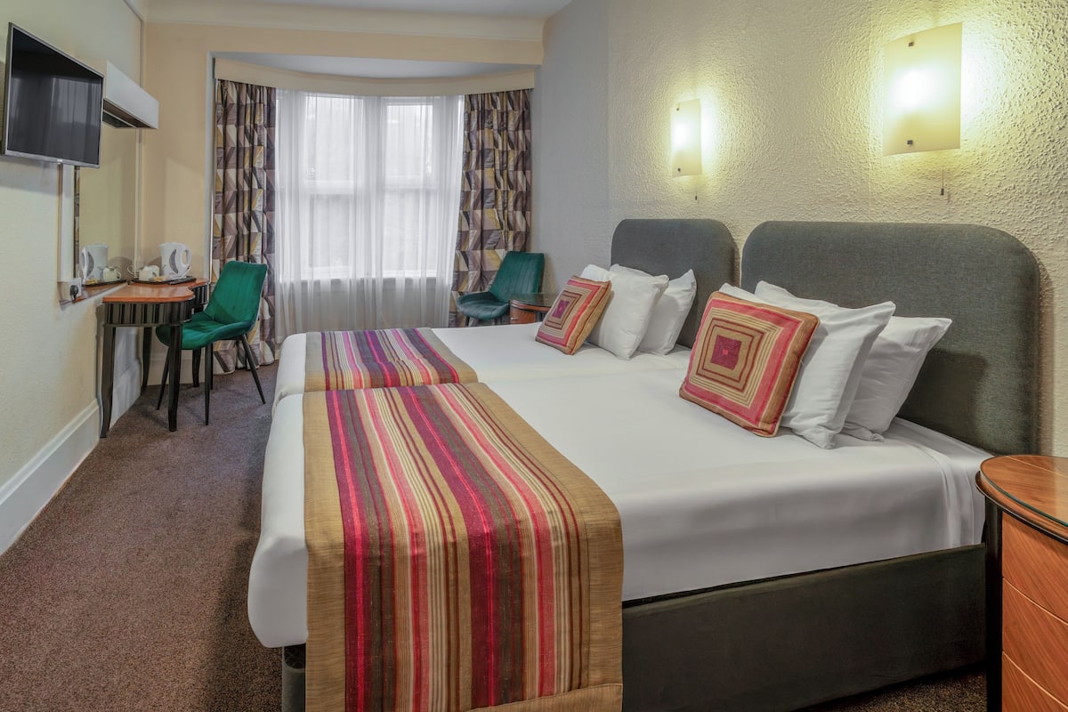 A hotel room with a large bed, two chairs, a desk with a chair, a TV, and a window with curtains.