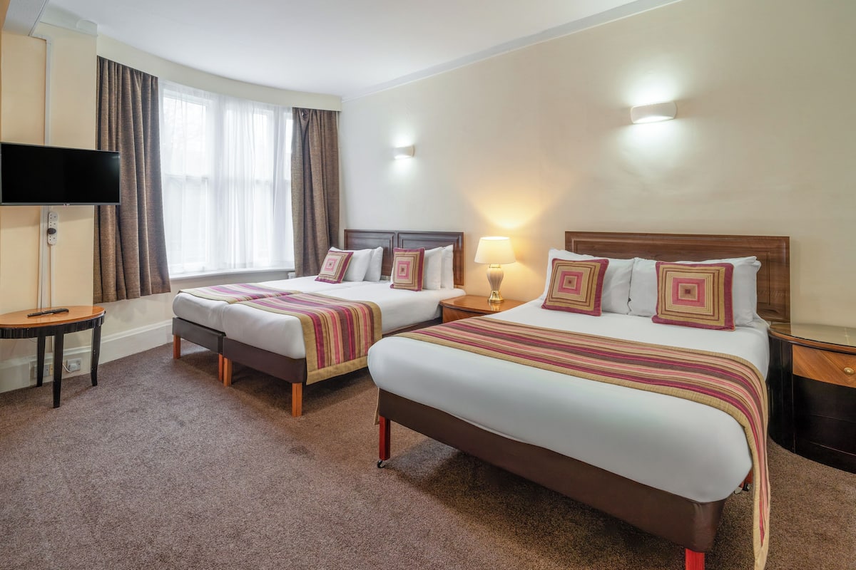 A hotel room with two beds, a TV, a lamp, and a window with curtains.
