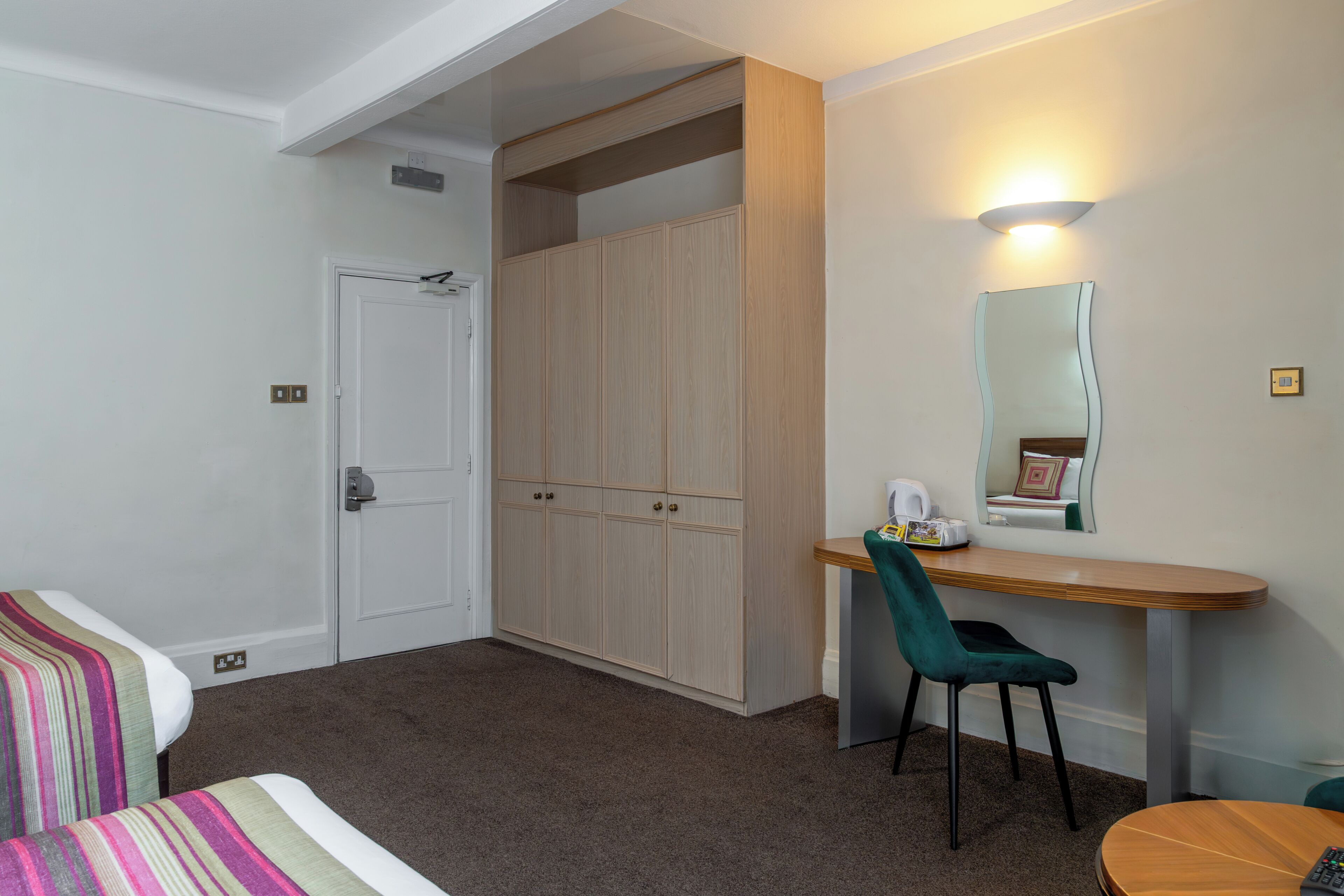 A room with a bed, a desk, a chair, a wardrobe, and a mirror.