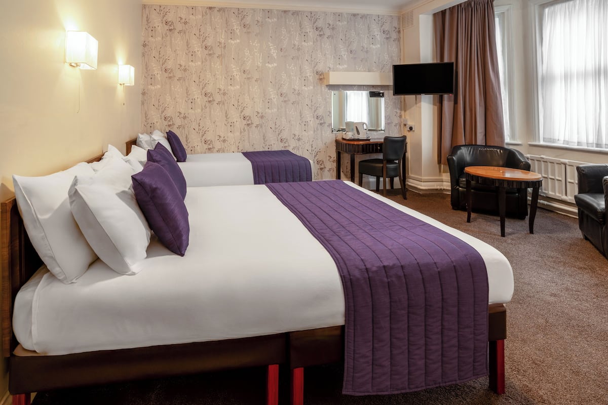 A hotel room with two beds, a desk, a chair, a TV, and a window with curtains.