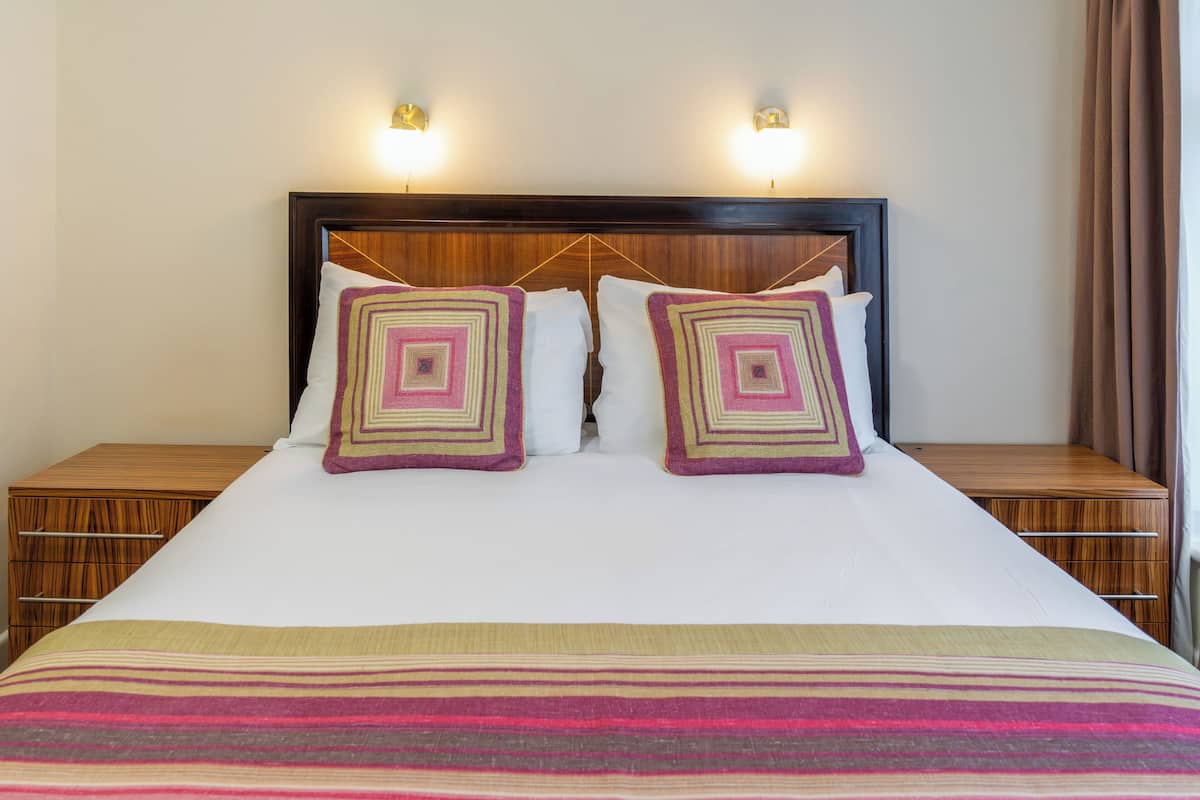 A neatly made bed with a striped blanket, two square pillows with a geometric pattern, and two bedside tables with wooden finishes.