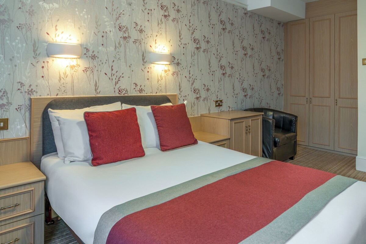 A neatly arranged hotel room with a bed, bedside tables, a desk, and a wardrobe.