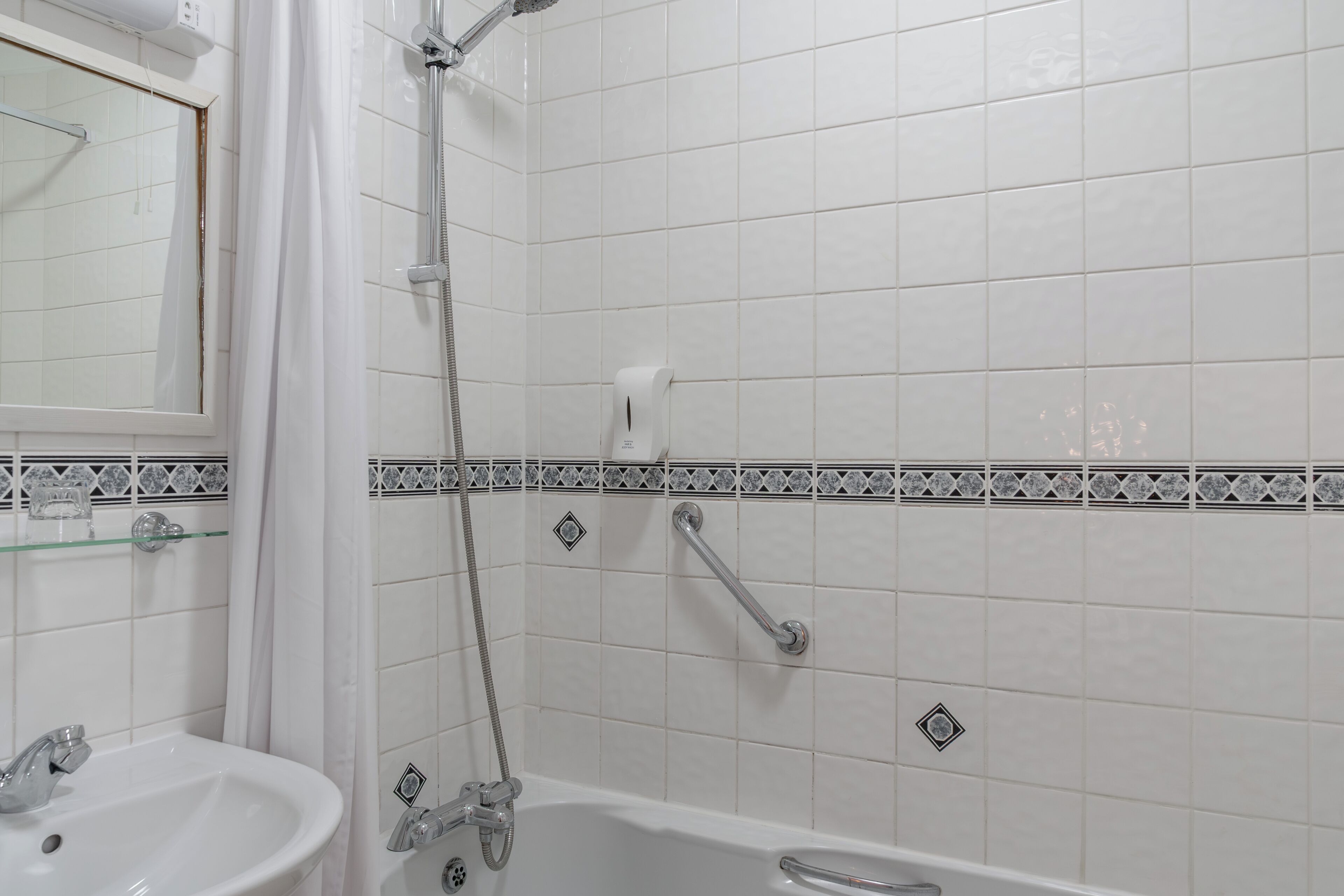 A bathroom with a white sink, a shower with a handheld showerhead, and a tiled wall with a decorative border.