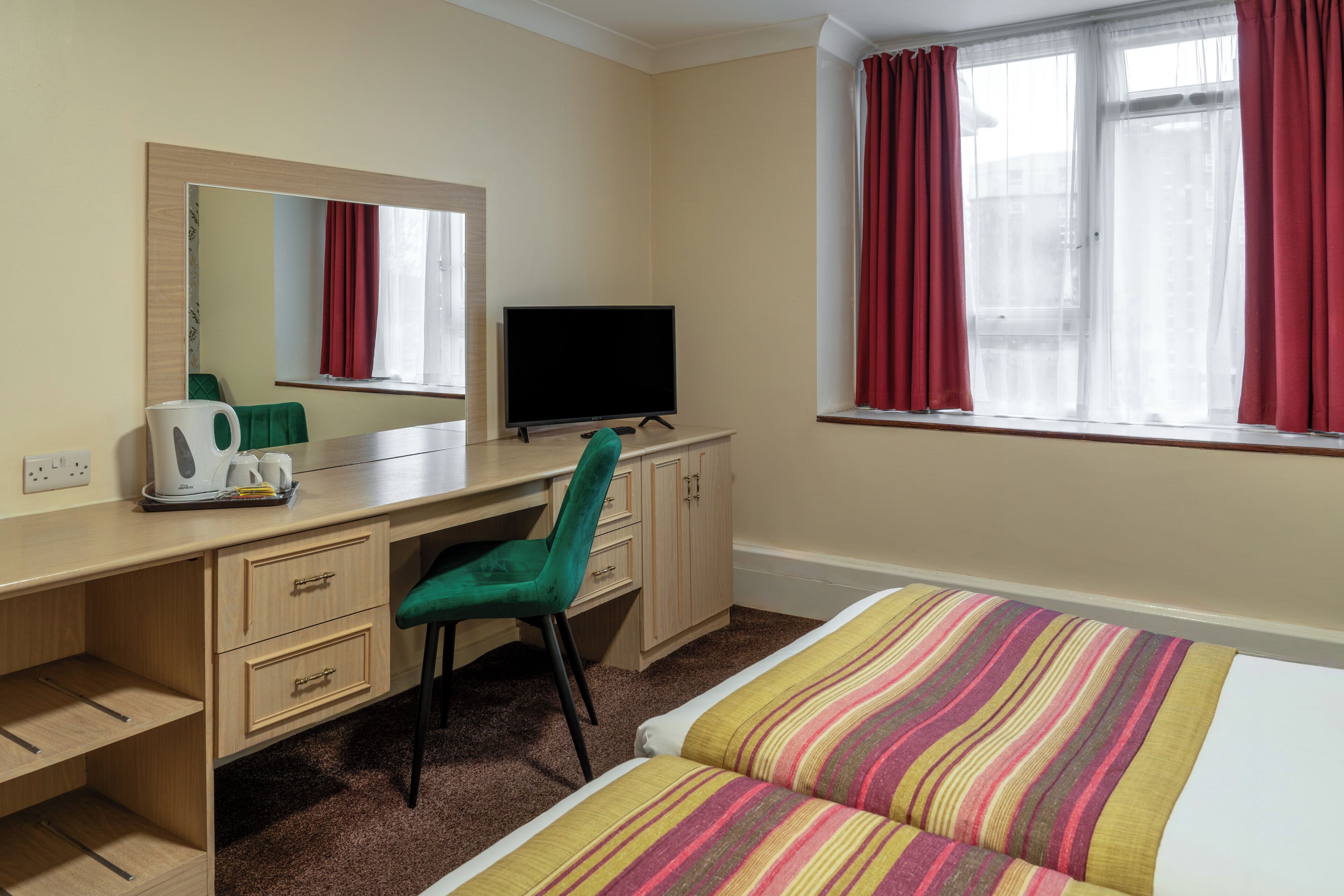 Una habitación de hotel con escritorio, silla, televisión, cama y ventana con cortinas.