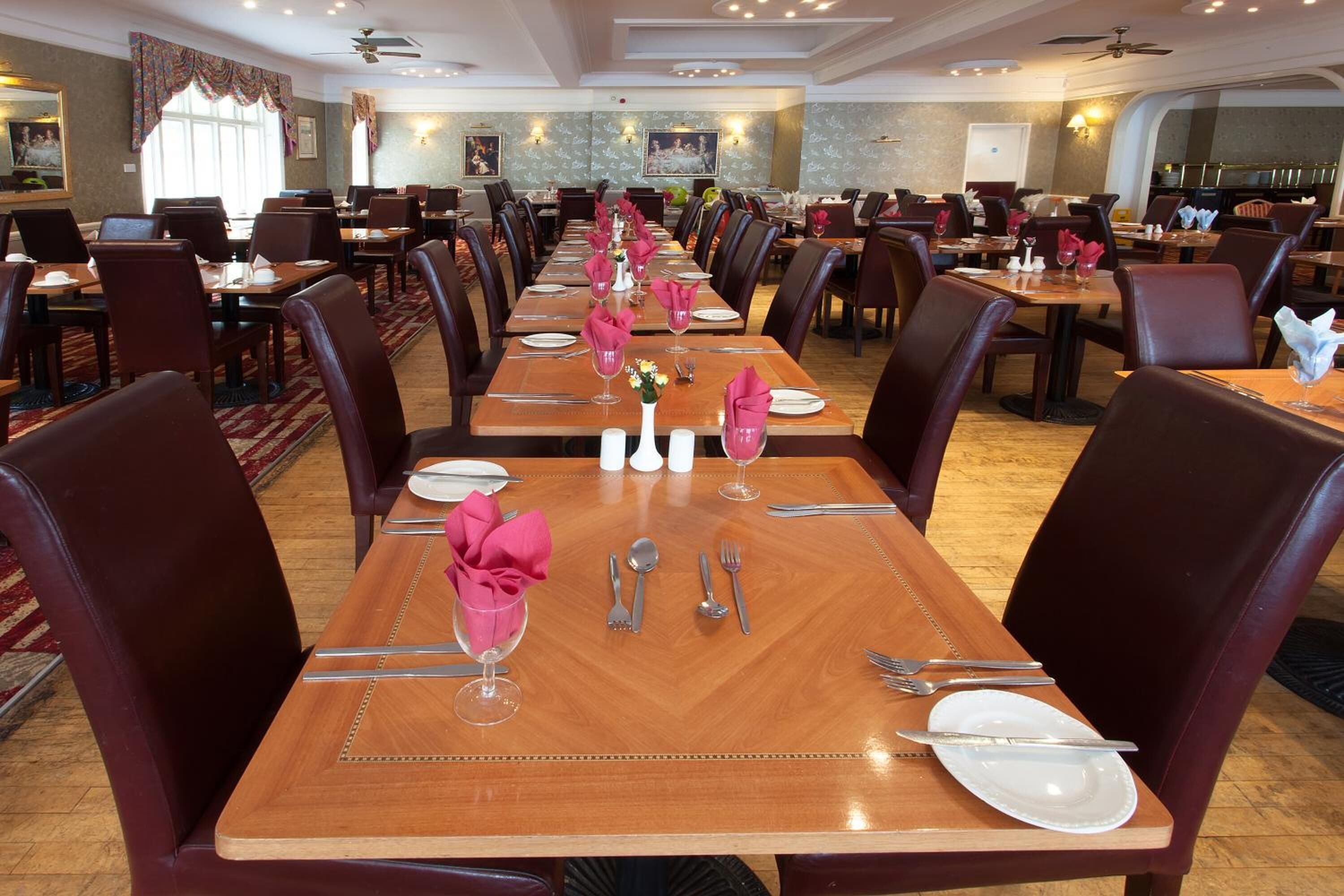 Un grand espace dédié à la salle à manger, avec plusieurs tables dressées pour le service, chacune agrémentée de couverts et de serviettes disposés avec soin.