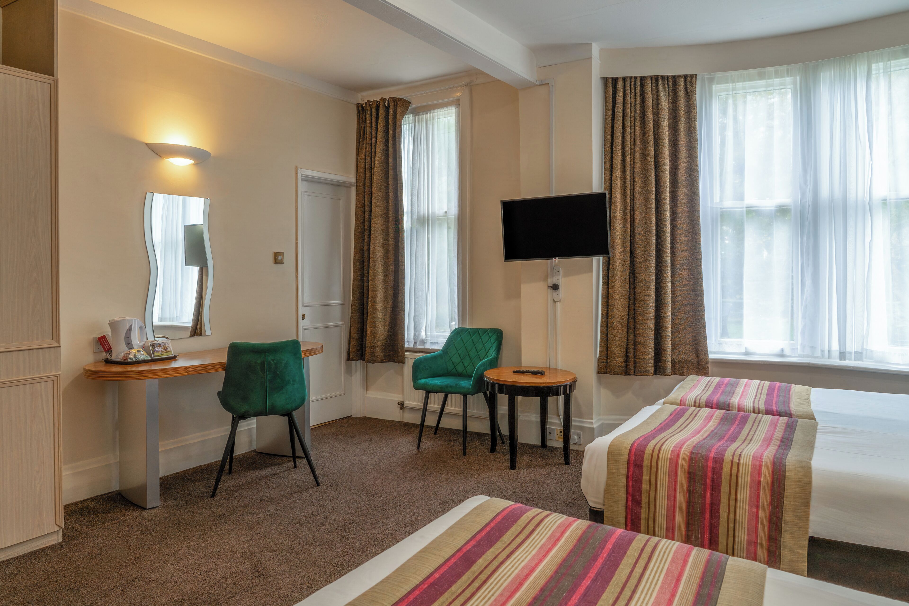Habitación de hotel con dos camas, un escritorio, una silla, un televisor y una ventana con cortinas.