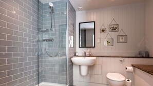 Une salle de bain moderne avec des murs recouverts de carreaux gris, une douche en verre, un lavabo blanc, des toilettes et des œuvres d’art décoratives sur les murs.
