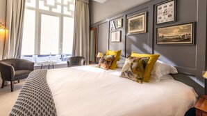 Une chambre d’hôtel avec un grand lit, deux chaises, une petite table et une fenêtre avec des rideaux.