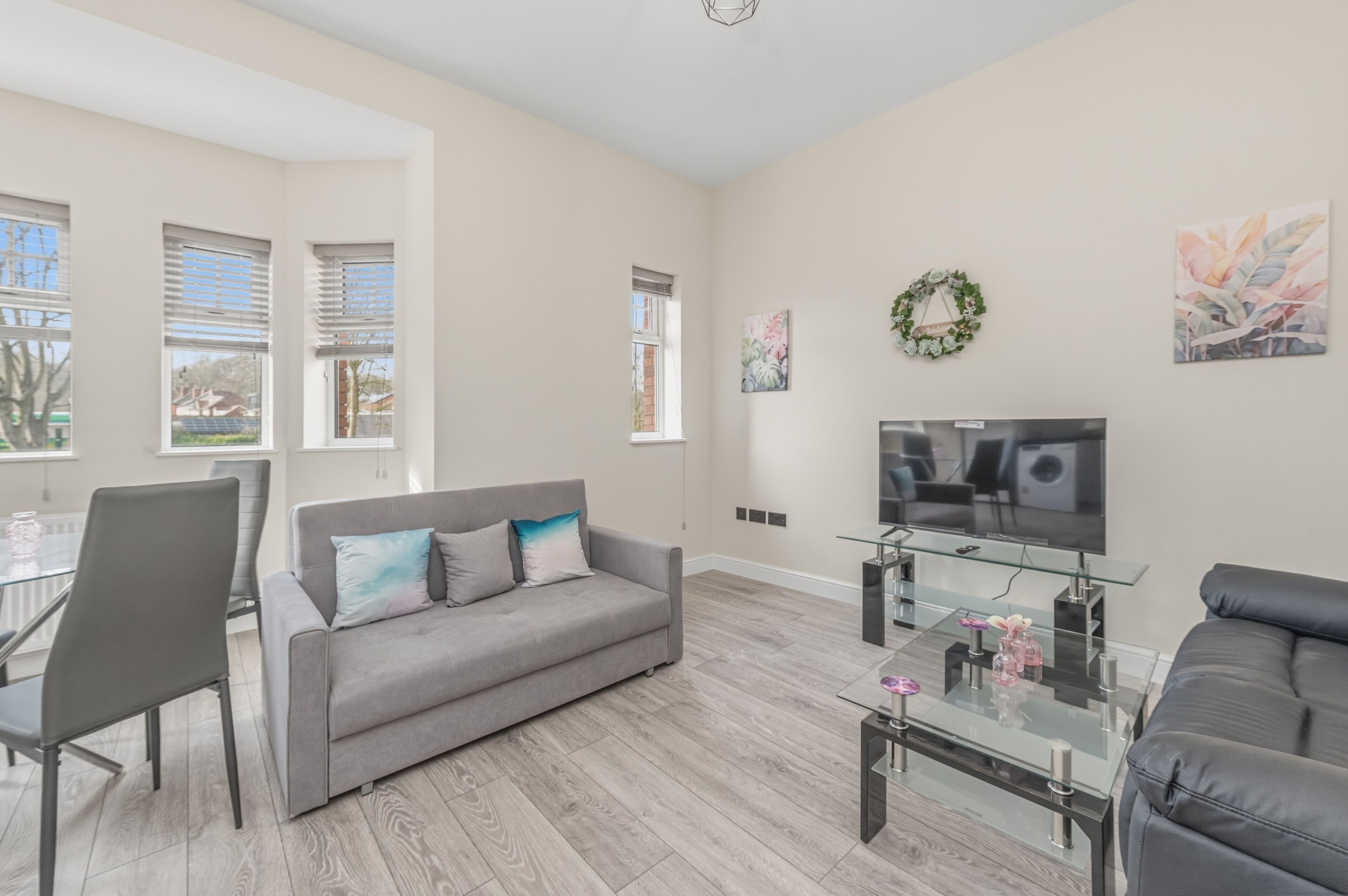 A modern living room with a grey sofa, a glass coffee table, a TV, and a dining area with chairs and a table.
