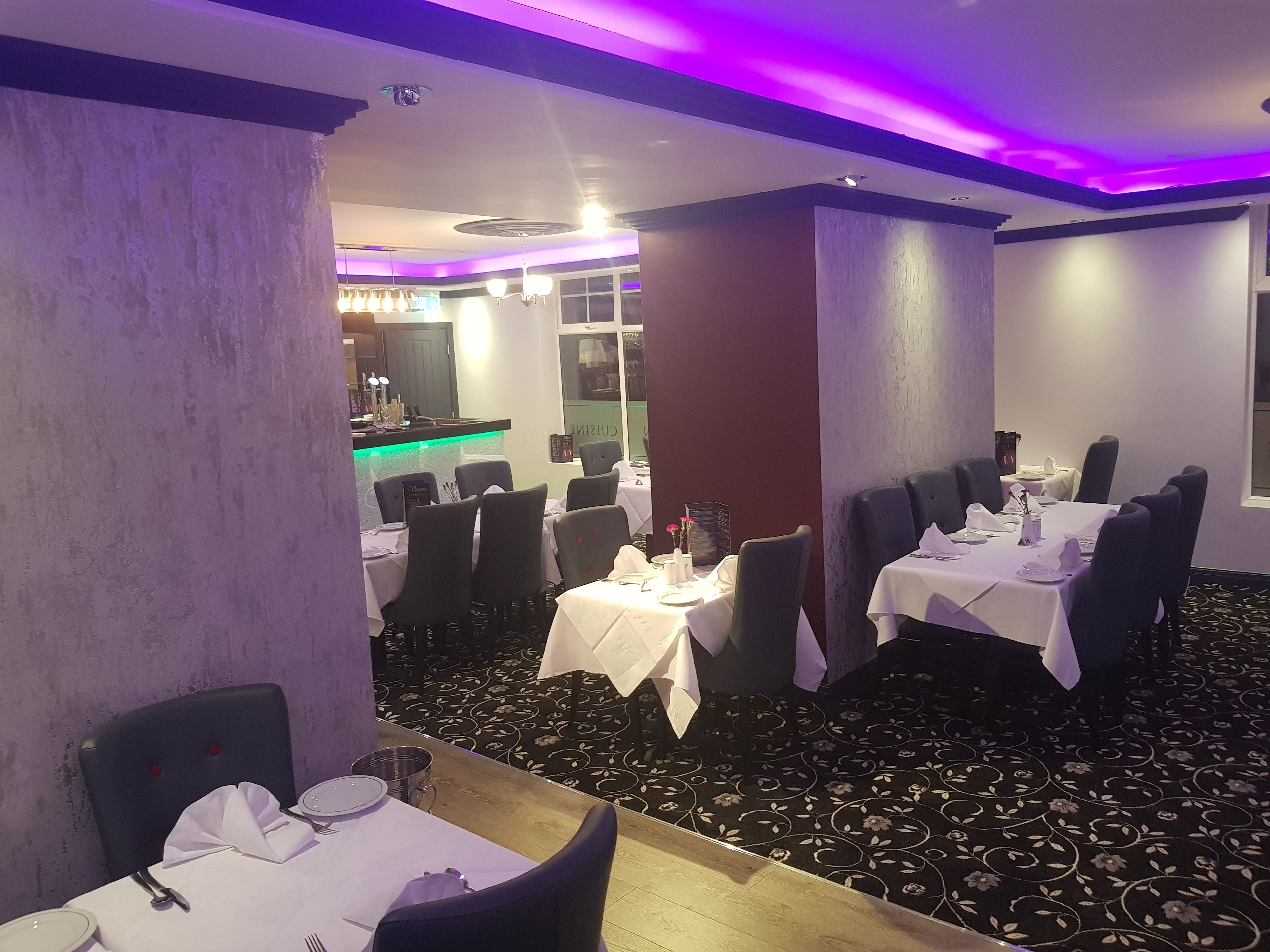 A dining area with tables set for four, chairs, and a bar area in the background.