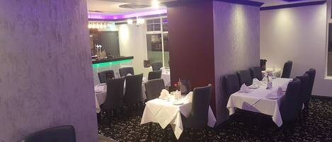 A dining area with tables set for four, chairs, and a bar area in the background.