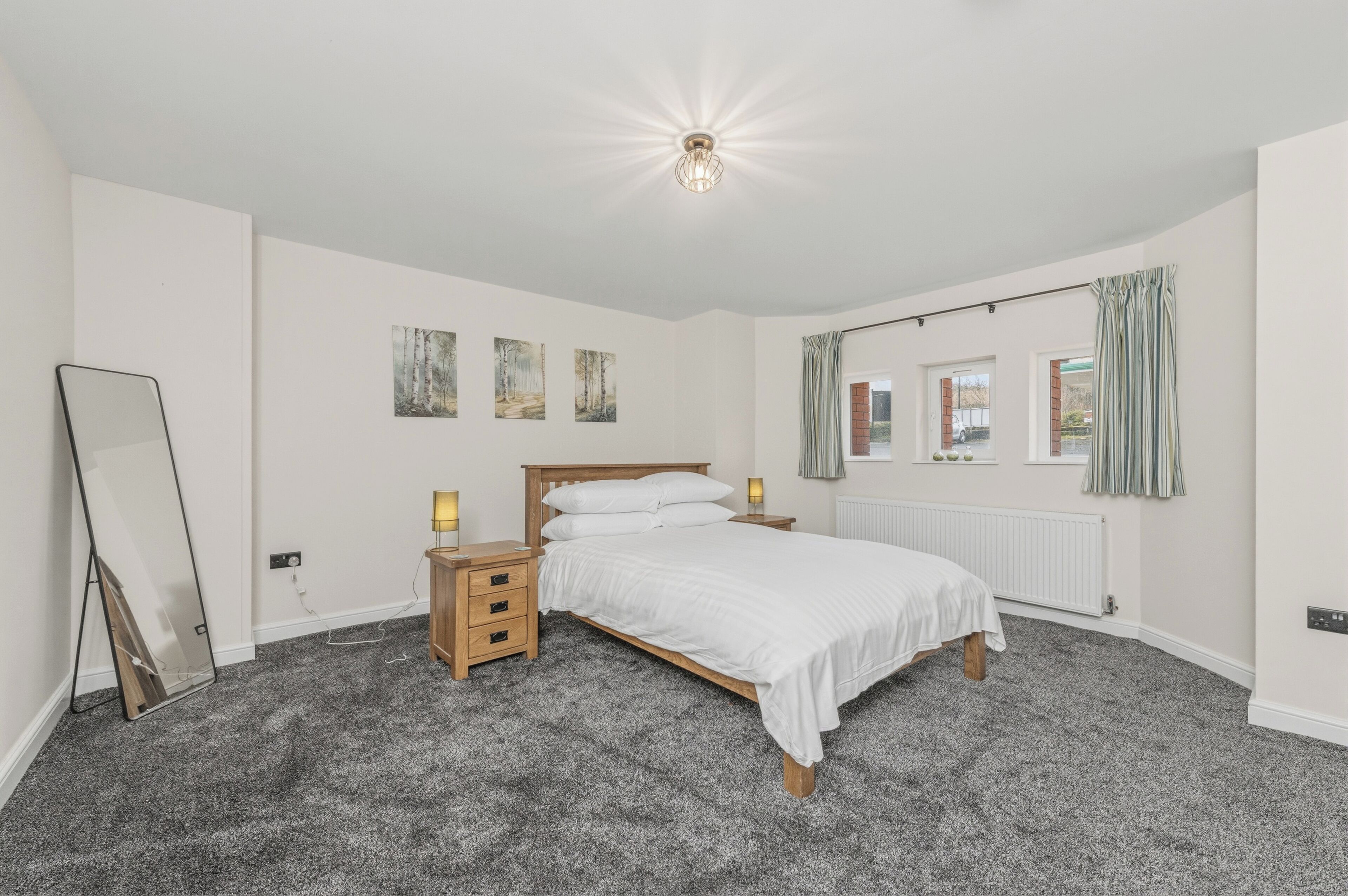 Une chambre à coucher avec un lit, des tables de chevet, un miroir, des œuvres d’art accrochées au mur et une fenêtre avec des rideaux.