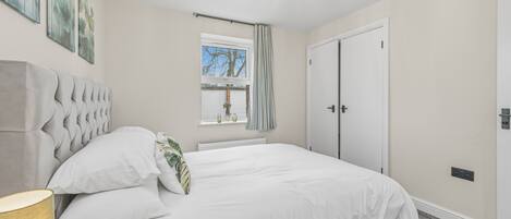 A bedroom with a bed, a window with curtains, a radiator, and a ceiling light fixture.