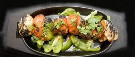 A dish of grilled chicken skewers with vegetables and herbs.