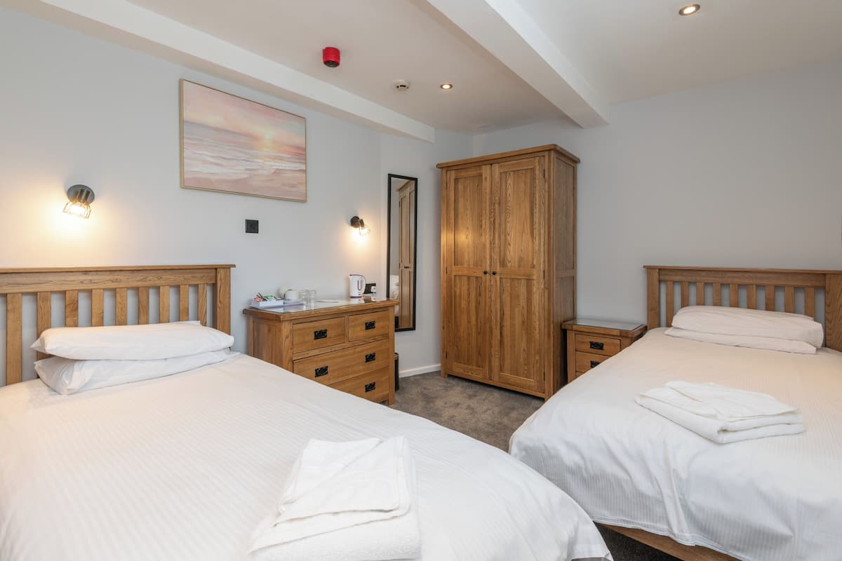 Habitación de hotel con dos camas, cabeceros de madera, un armario, una mesita de noche y un velador.