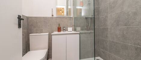 Un baño moderno con inodoro, lavamanos, cabina de ducha de vidrio y un mueble con artículos de aseo.