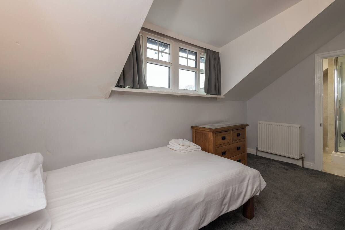 Un dormitorio con una cama individual, un aparador de madera, una ventana con cortinas y un radiador.