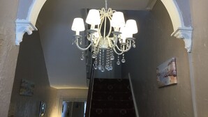 A chandelier with multiple lamps and crystal decorations hanging from a ceiling in a room with a high arched doorway and a patterned carpet. - Newburgh Guesthouse (Torquay)