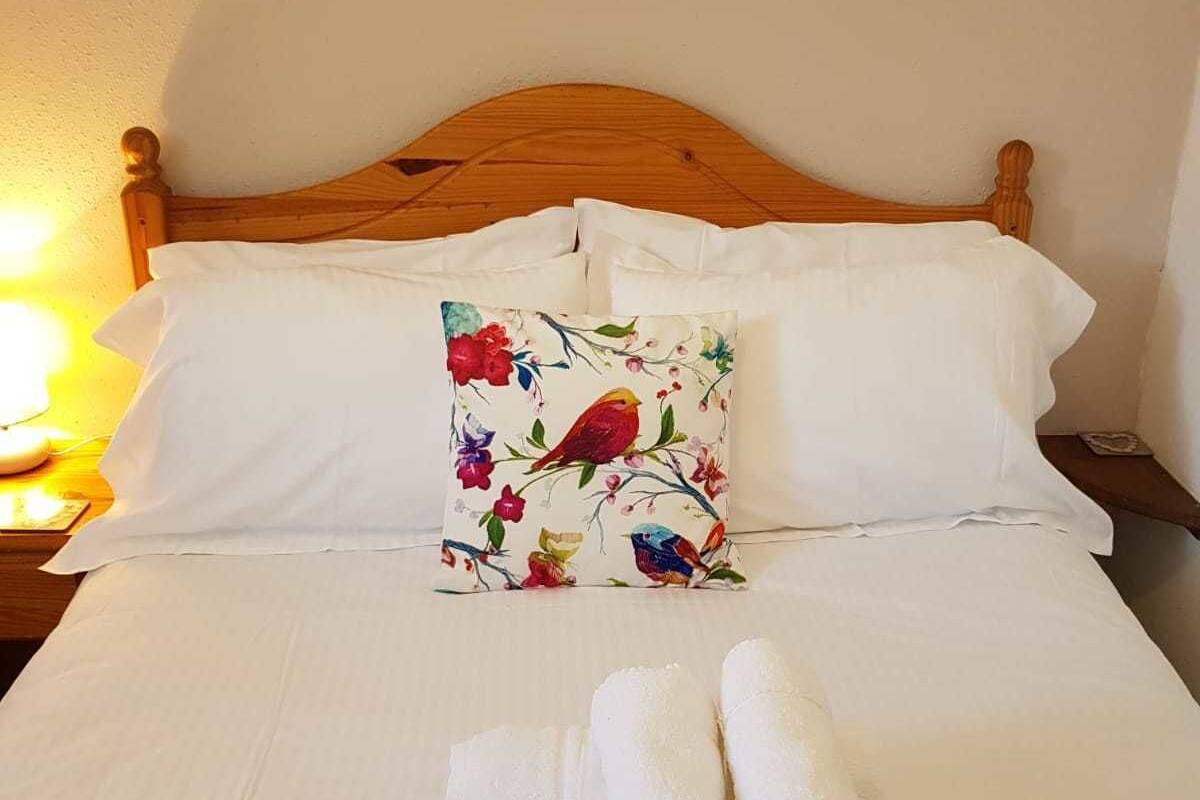 Una cama bien hecha con sábanas blancas, un cojín floral y toallas enrolladas.