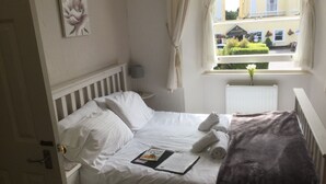 A neatly made bed with white linens, a pillow, and a folded towel. A magazine titled "Facing Our" is placed on the bed. - Newburgh Guesthouse (Torquay)