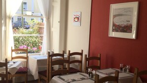 A dining area with tables and chairs, a window with curtains, a red wall, and a framed picture. - Newburgh Guesthouse (Torquay)