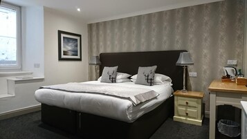 A neatly arranged hotel room with a large bed, bedside tables, a desk, and a trash bin.