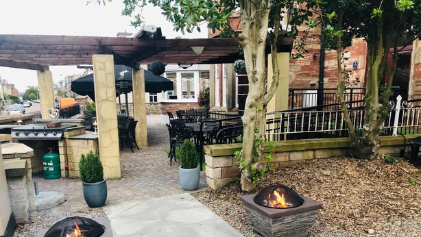 An outdoor patio area with stone tables and chairs, a fire pit, and a covered seating area. - The Redcliffe (Inverness)