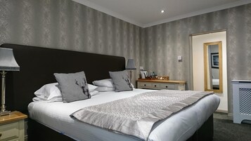 Cama bem arrumada com colcha estampada, mesa de cabeceira com abajur e criado-mudo.