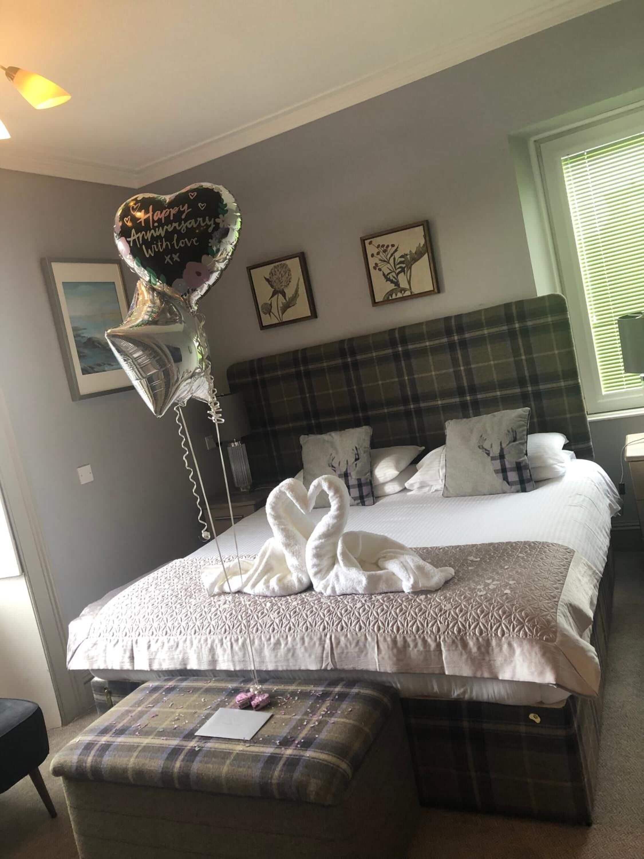 A hotel room with a bed, a bench, and a heart-shaped balloon.