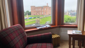 A room with a plaid armchair, a radiator, and a table with a book. - The Redcliffe (Inverness)