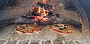 Dos pizzas horneándose en un horno de ladrillo con fuego a sus espaldas.