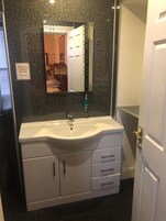 Un baño con un lavamanos blanco, un espejo y una puerta con un letrero que dice 'Cierre la puerta del baño al ducharse'.