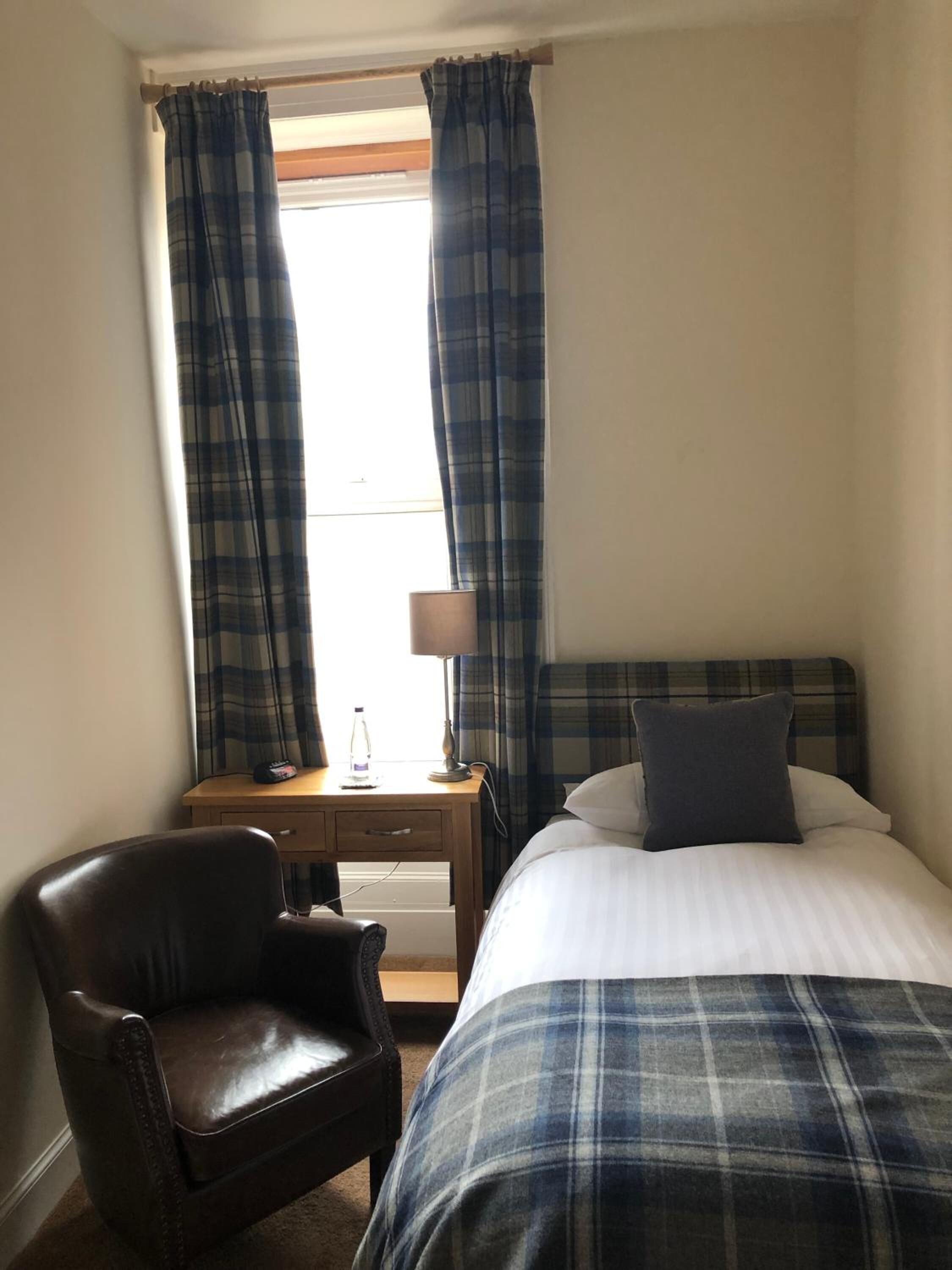 Une chambre d’hôtel avec un lit, une chaise, un bureau avec une lampe et des rideaux.