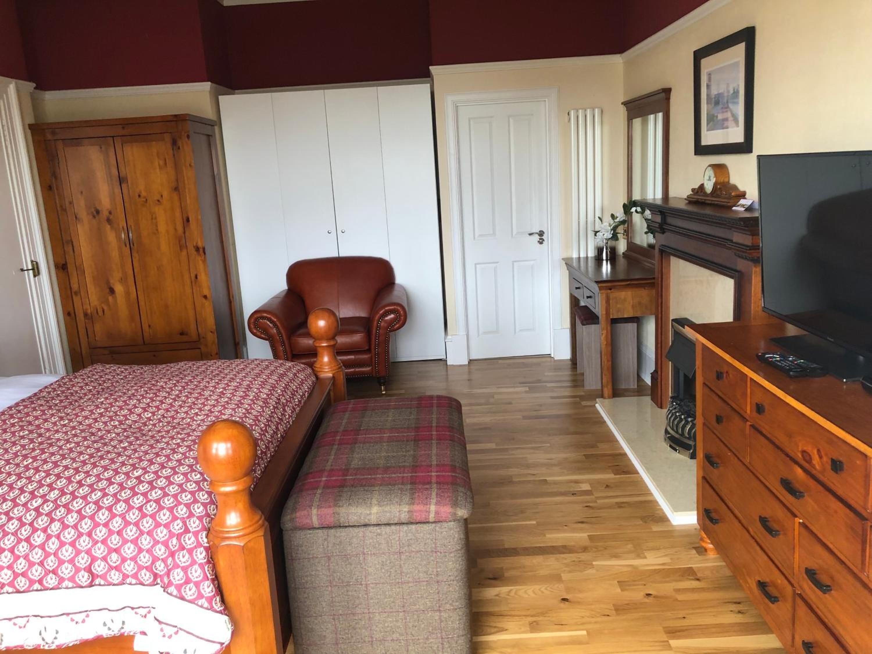 Ein Schlafzimmer mit Bett, Sessel, Kommode und Schreibtisch mit Fernseher.