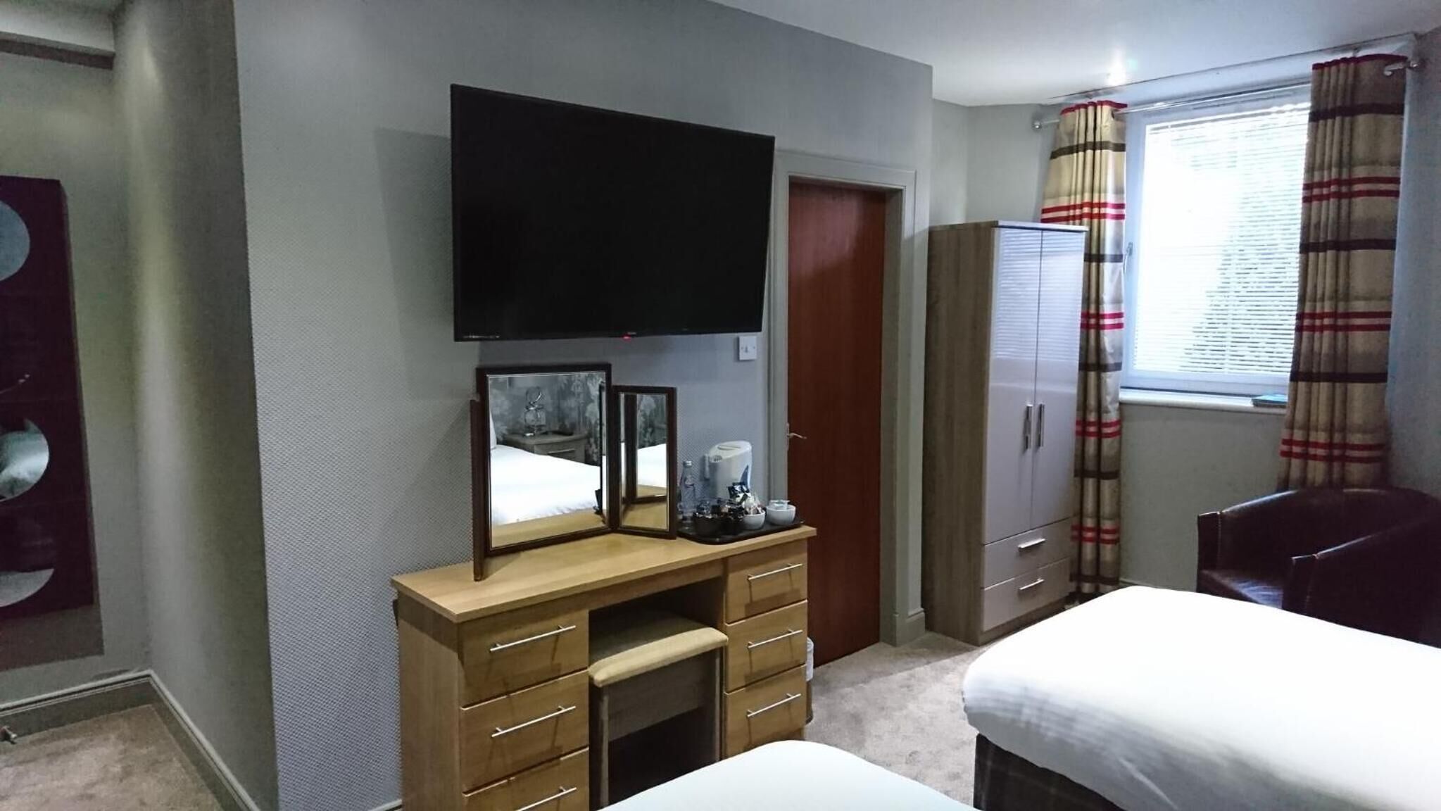 Une chambre d’hôtel avec un lit, un téléviseur fixé au mur, une armoire et une fenêtre avec des rideaux.
