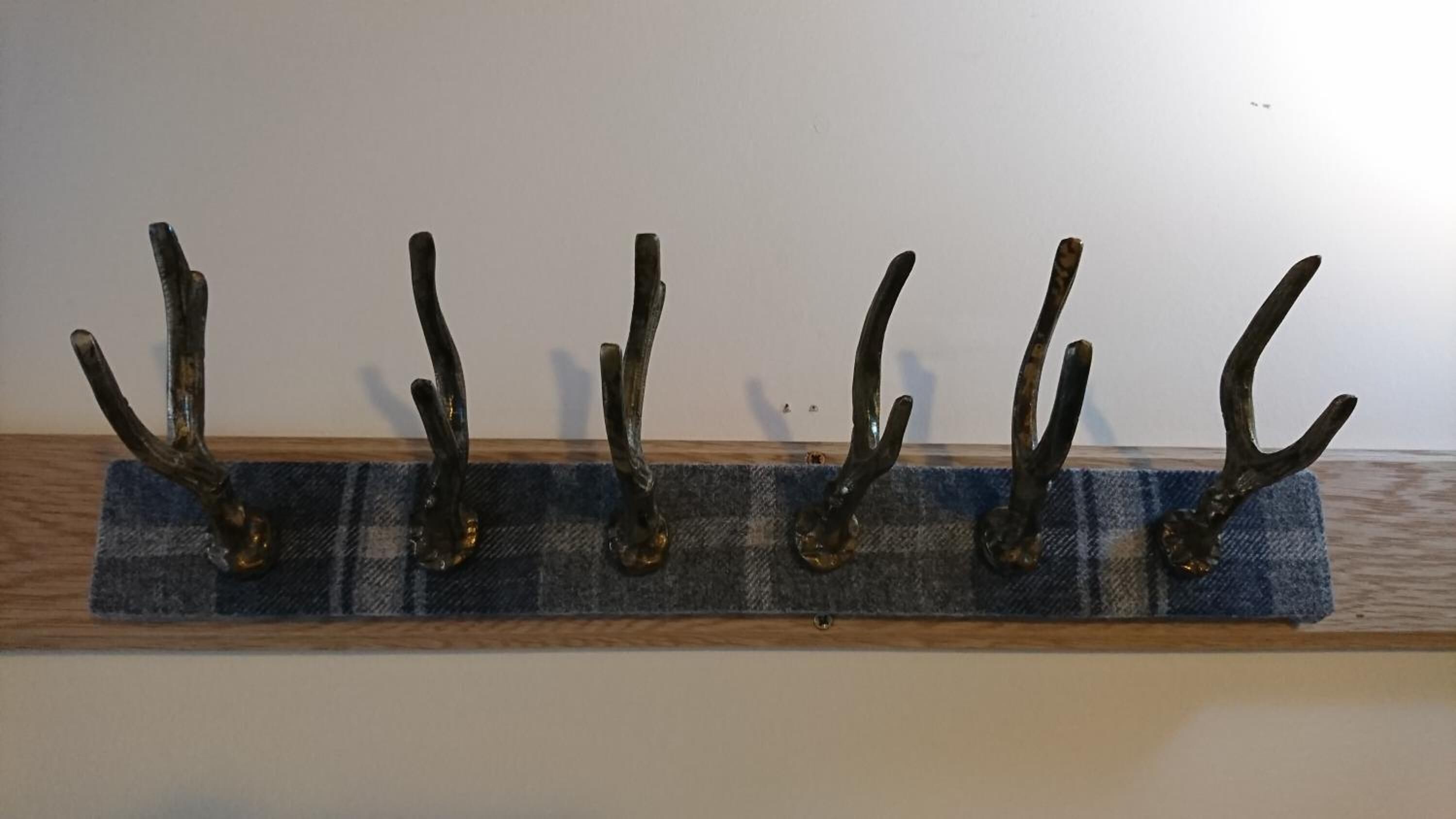 A wall-mounted rack with five metal hooks on a blue plaid fabric.