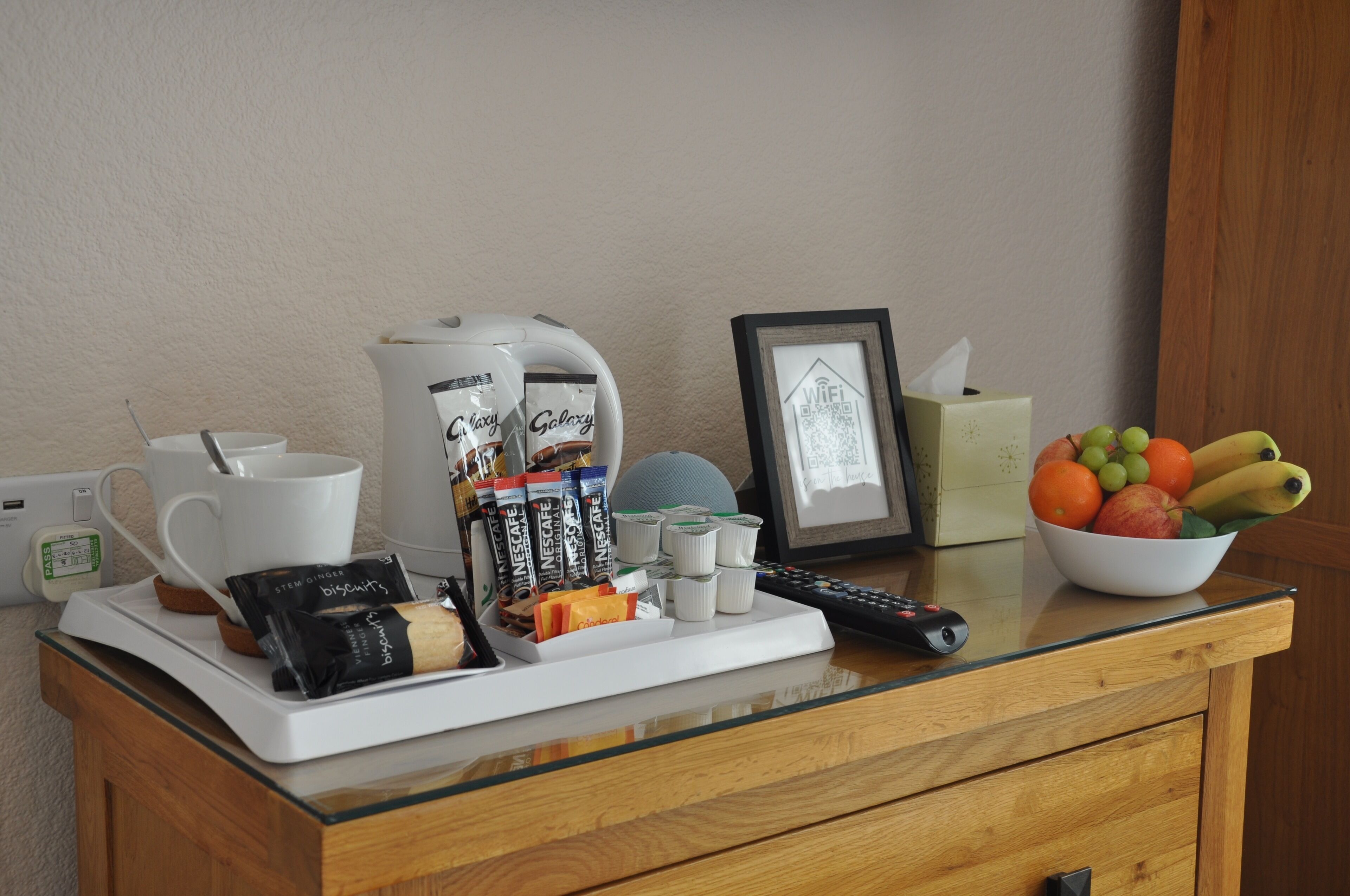 A breakfast tray with coffee, tea, snacks, and a bowl of fruit on a hotel counter.