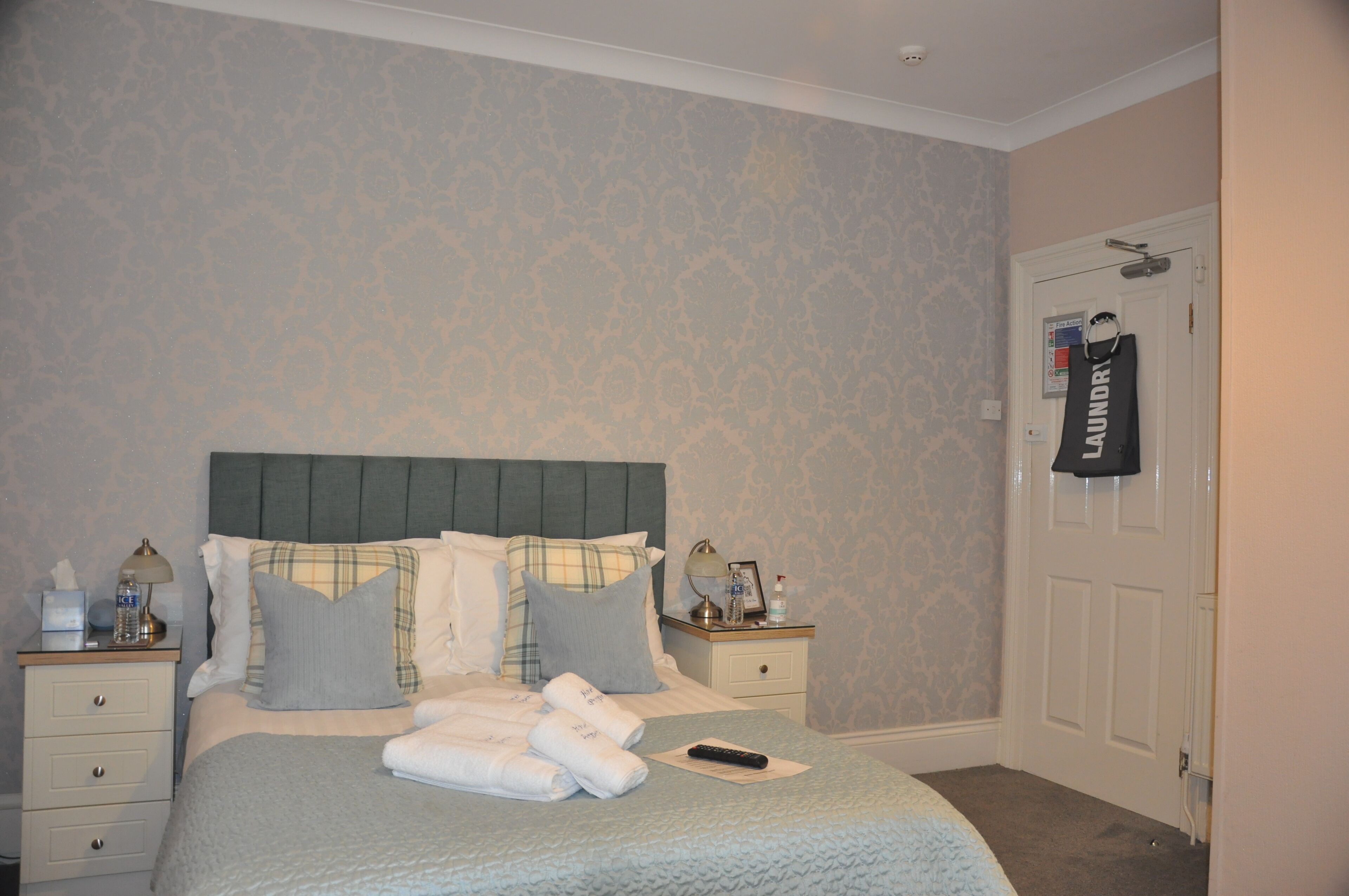 A neatly made bed with a plaid headboard, two bedside tables with lamps, and a door with a laundry bag hanging on it.
