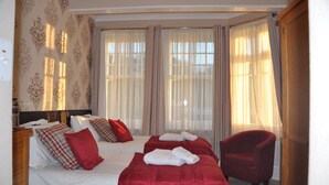 A hotel room with two beds, red and white bedding, a red armchair, and a large window with curtains. - Hotel Peppers (Torquay)