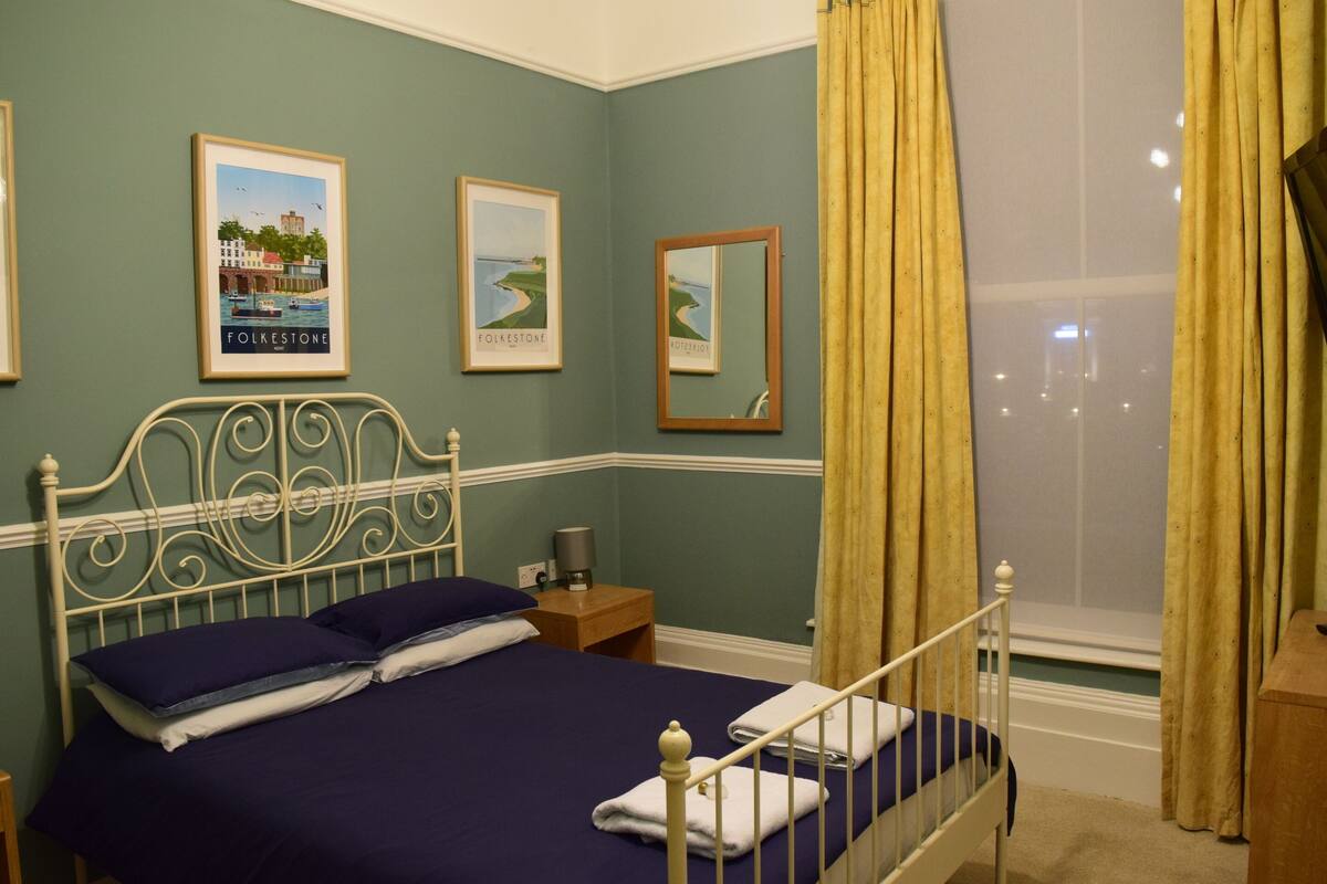 A neatly made bed with a headboard, a bedside table with a lamp, and two framed pictures on the wall.