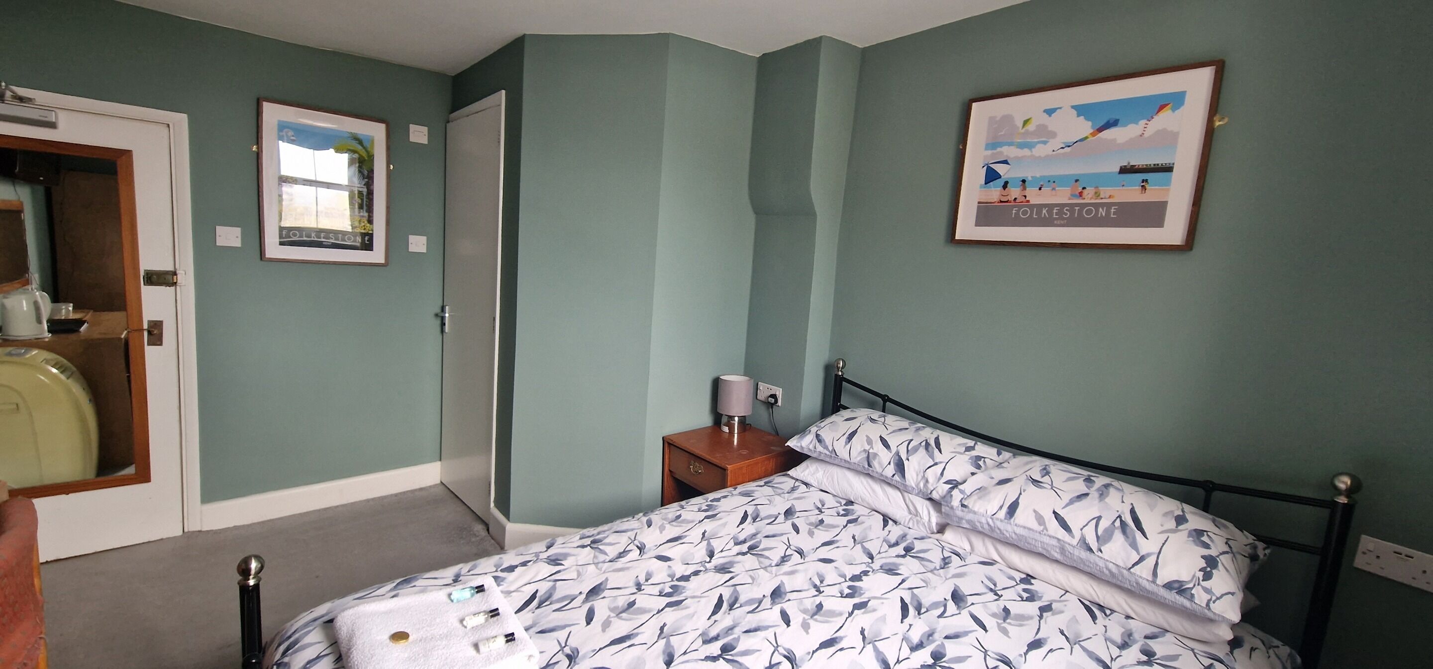 A bedroom with a bed, a nightstand, a framed picture, and a door.