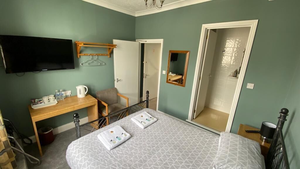 Ein Schlafzimmer mit einem Bett, einem Schreibtisch, einem Sessel, einem Fernseher und einem Spiegel.
