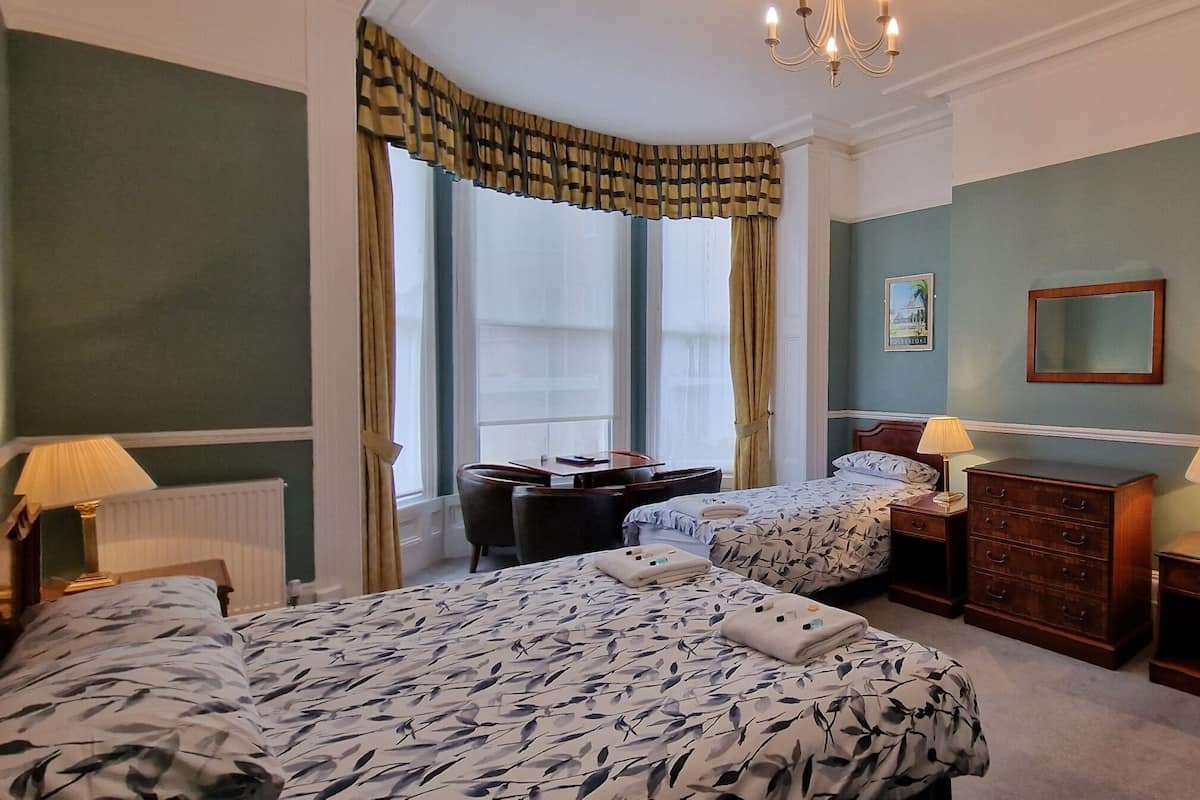 A hotel room with two beds, a dresser, a chair, a desk, a mirror, and a window with curtains.