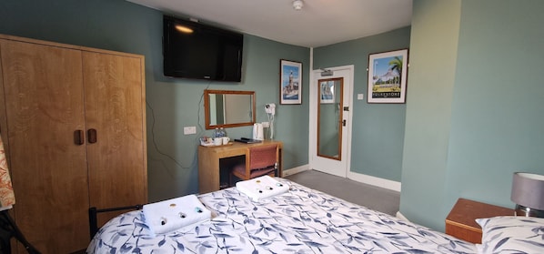 A hotel room with a bed, a wooden wardrobe, a desk with a mirror, a telephone, and a television mounted on the wall. - Portland Hotel (Folkestone)