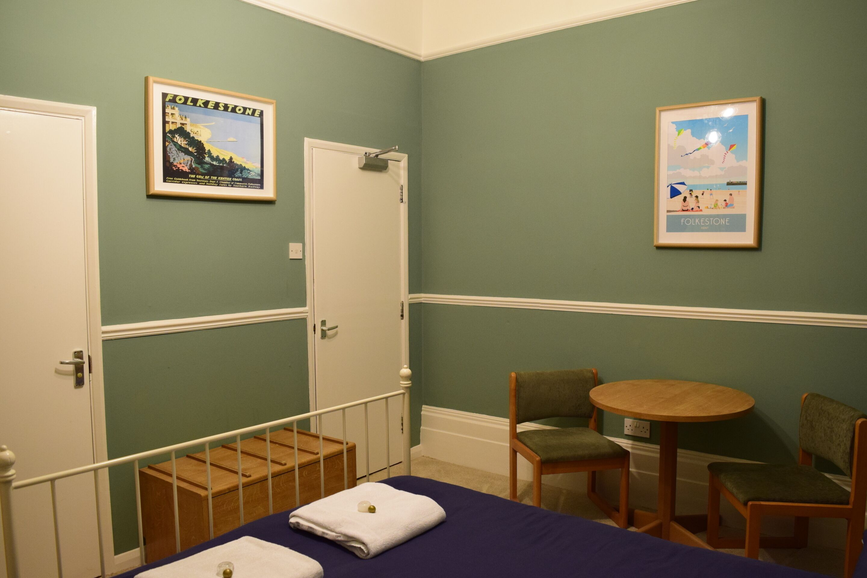 Una habitación con una cama, dos sillas, una mesita y dos cuadros en la pared.