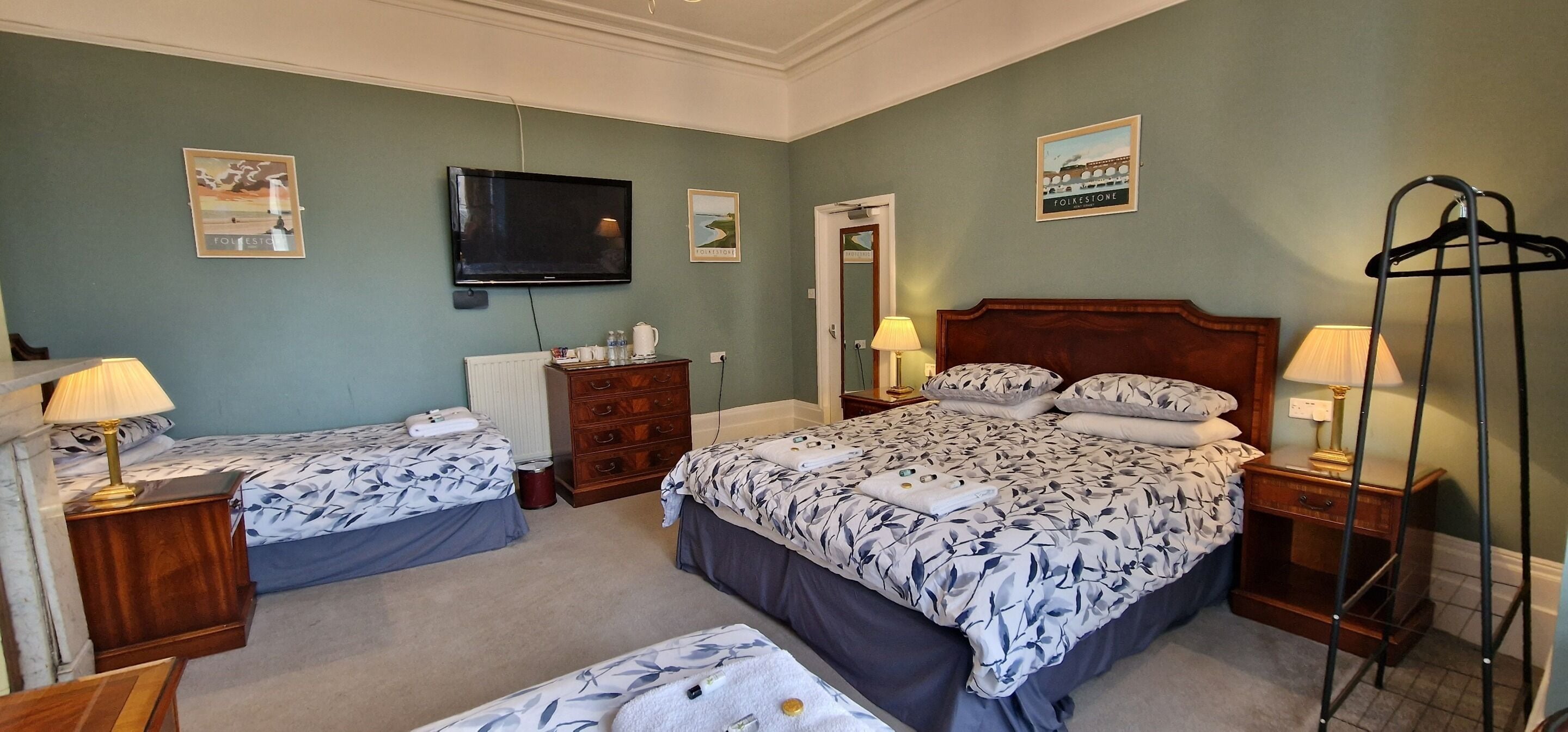Habitación de hotel con dos camas, televisión, cómoda, radiador y perchero.