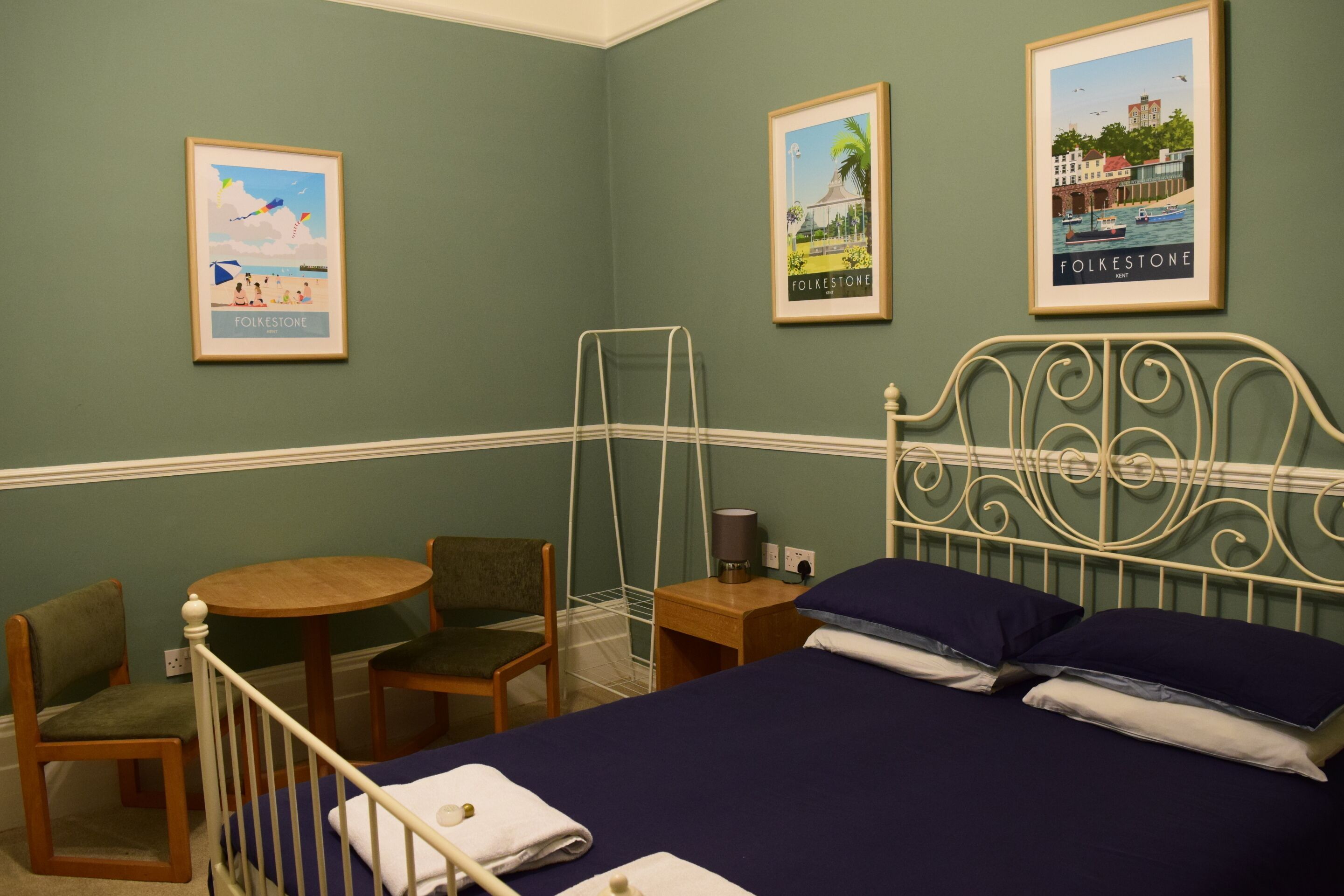 Une pièce comprenant un lit, une chaise, une petite table et deux tableaux encadrés accrochés au mur.