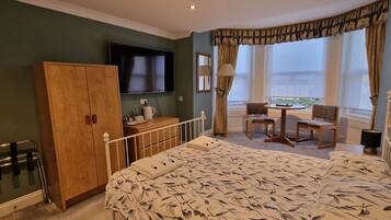 A hotel room with a bed, a wooden wardrobe, a television, a small table with chairs, and a window with curtains.