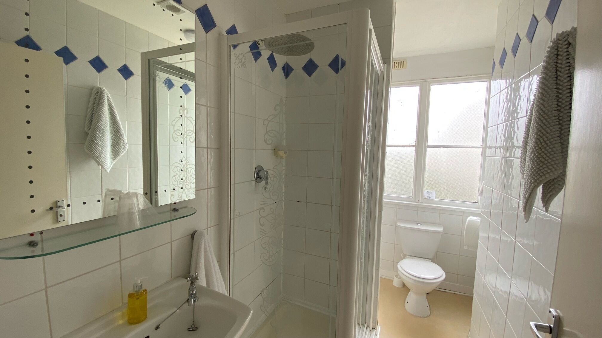 Un baño con cabina de ducha de vidrio, inodoro, lavabo con repisa de vidrio y espejo.