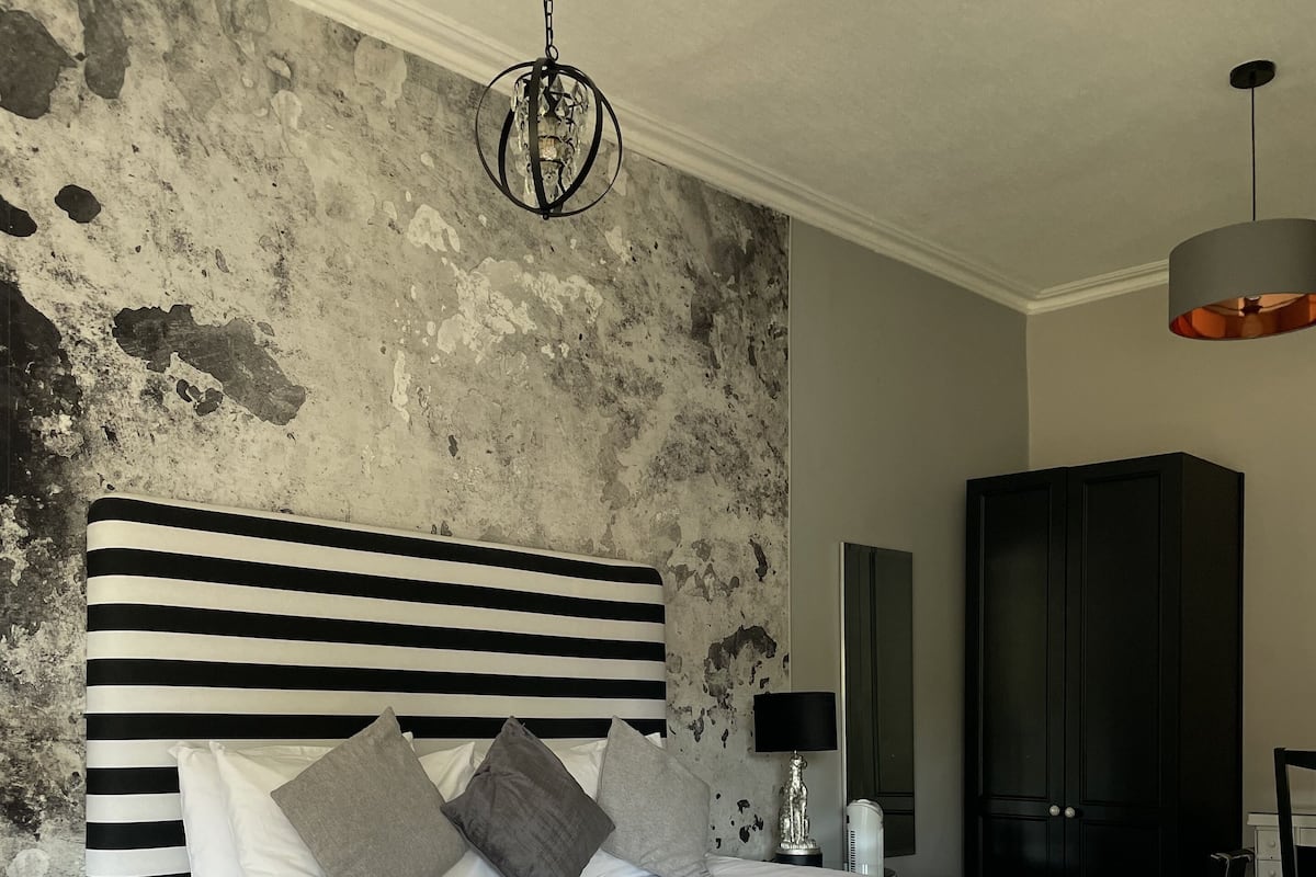 A bedroom with a large bed, a modern chandelier, a dark wardrobe, and a textured wall.